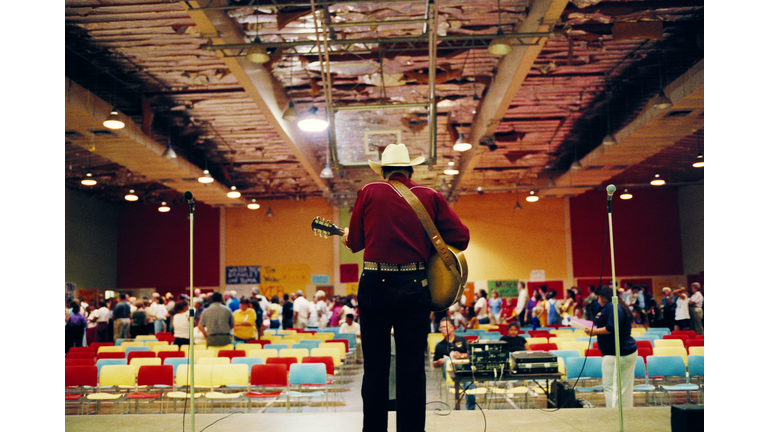 Man wearing cowboy hat, playing guitar in auditorium, rear view