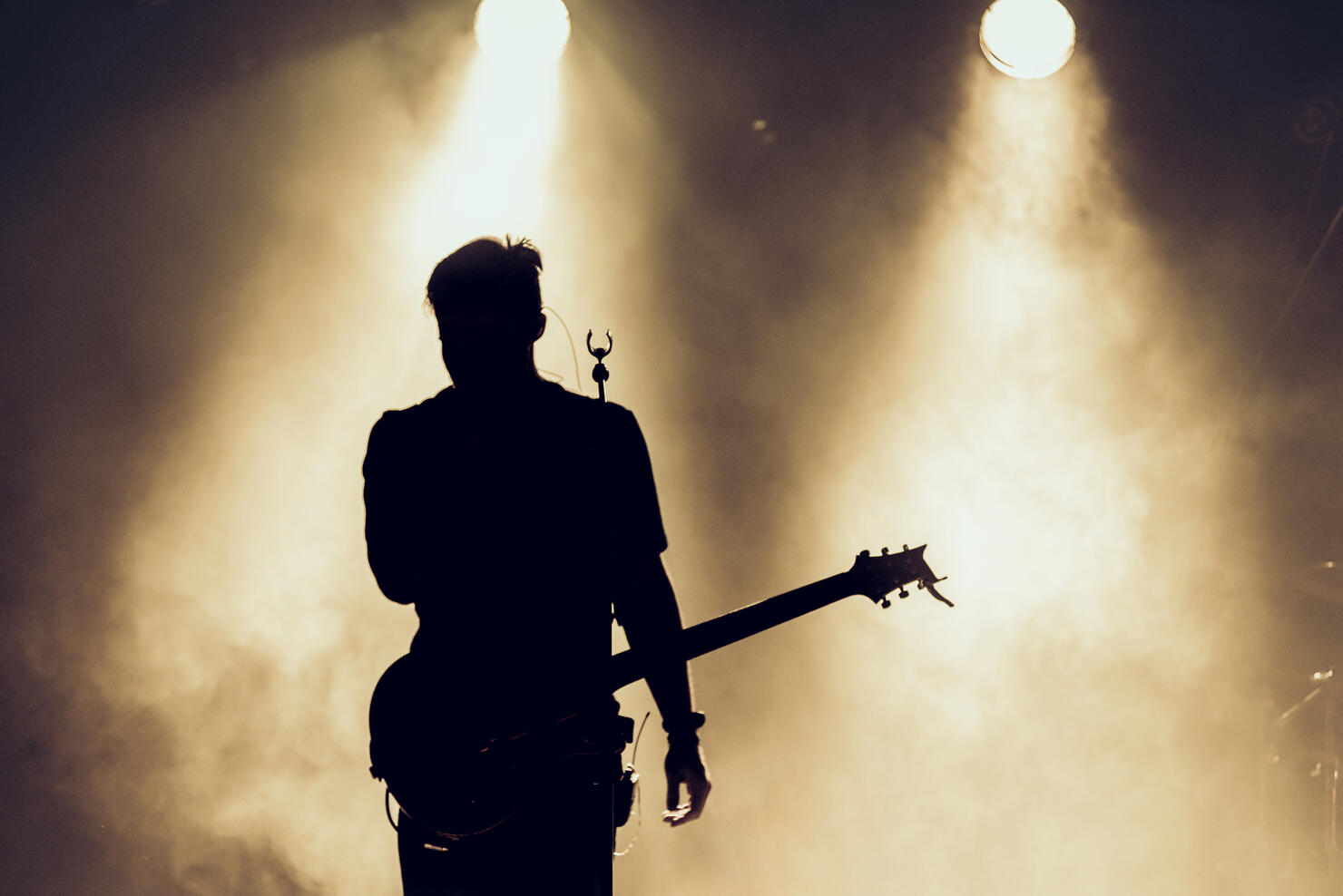 Rock band performs on stage. Guitarist plays solo. silhouette of guitar player in action on stage behind lights.