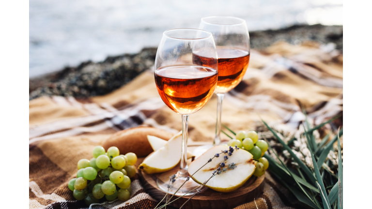 Two glasses of wine and summer fruits on the beach, sea and landscape in background, summer picnic, idea for outdoor weekend activity