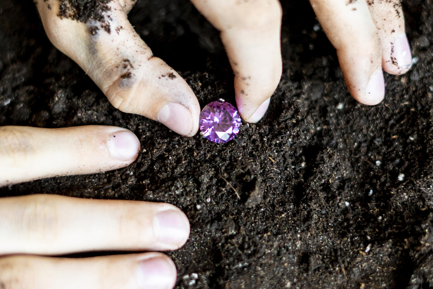 searcher hands holding a diamond in the soil ground f