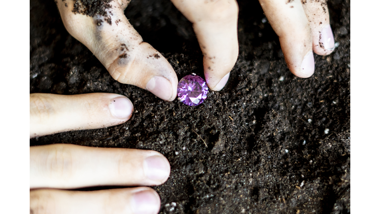 searcher hands holding a diamond in the soil ground f