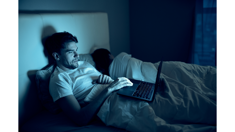 A man and a woman sleep in the same bed, and a man browses adult sites on the Internet at night.