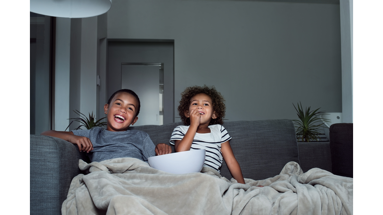 Happy siblings having popcorn while watching TV