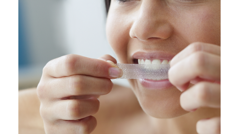 Close up of young woman using a teeth whitening strip