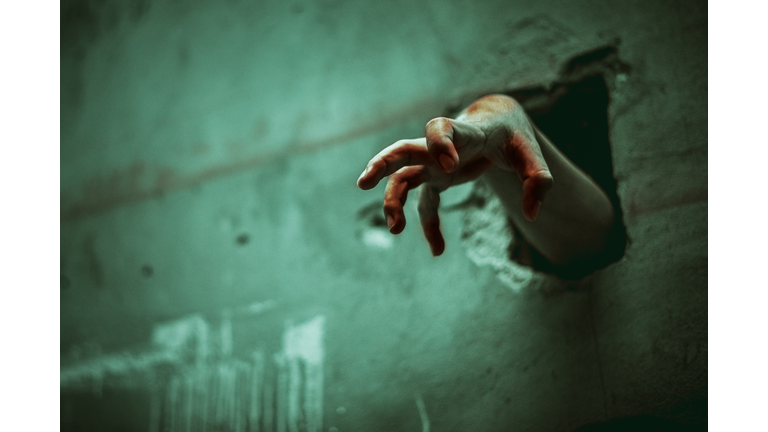 Zombie hand through the cracked wall. Horror and scary film concept. Halloween day theme. Green tone like ghost movie
