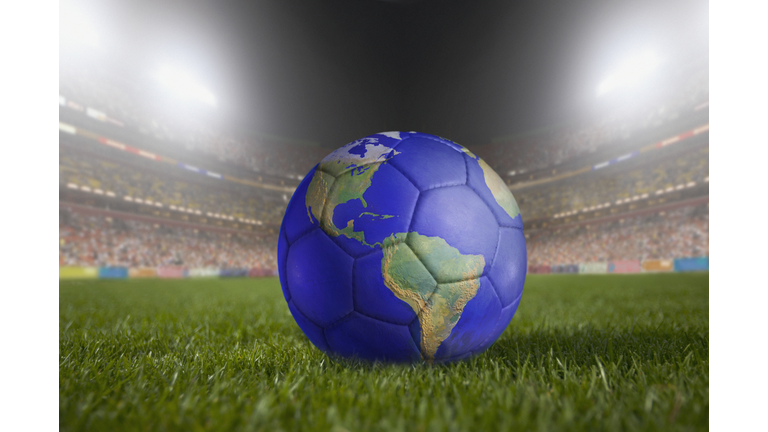 Soccer ball painted like a globe resting on grass in large stadium