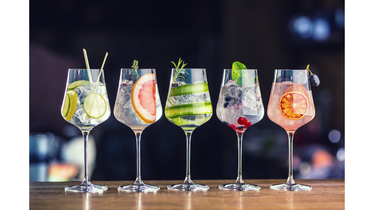 Five colorful gin tonic cocktails in wine glasses on bar counter in pup or restaurant
