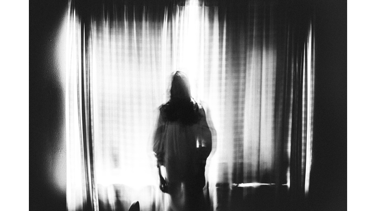 Spooky image of ghost girl standing in window in eery light