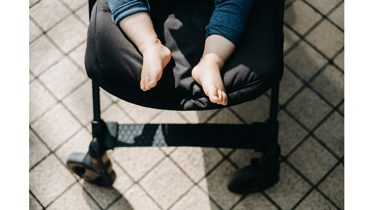 Low section of baby feet resting in baby stroller on street with warmth of sunlight