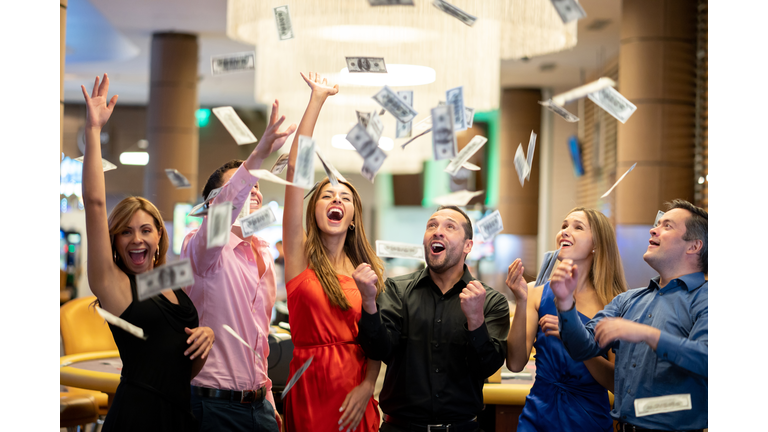 Group of friends at the casino celebrating a big win throwing money to the air