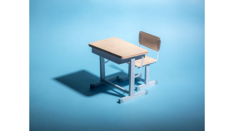 Empty school desk on a blue background. Conceptual.