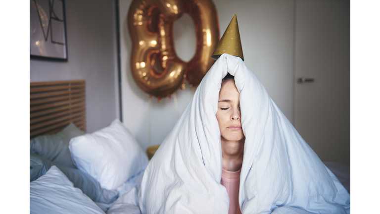 Sad woman celebrating her birthday, sitting on bed under blanket