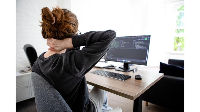 A woman holding her neck while working on computer sitting at desk at home