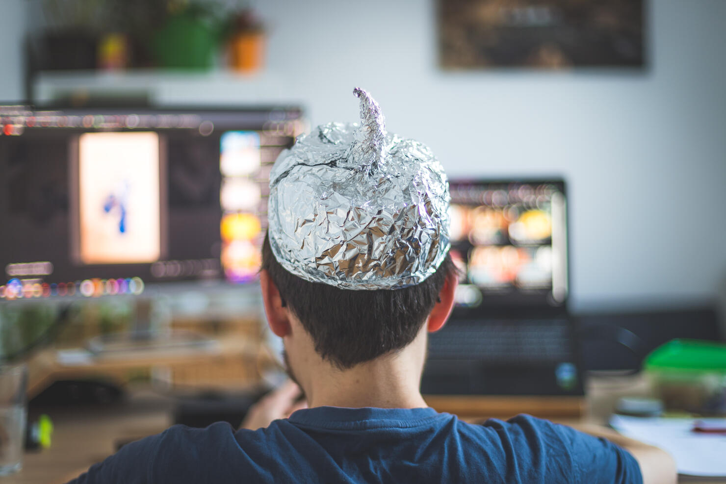 Conspiracy theory concept: young man is wearing aluminum head, sitting in front of the pc watching videos