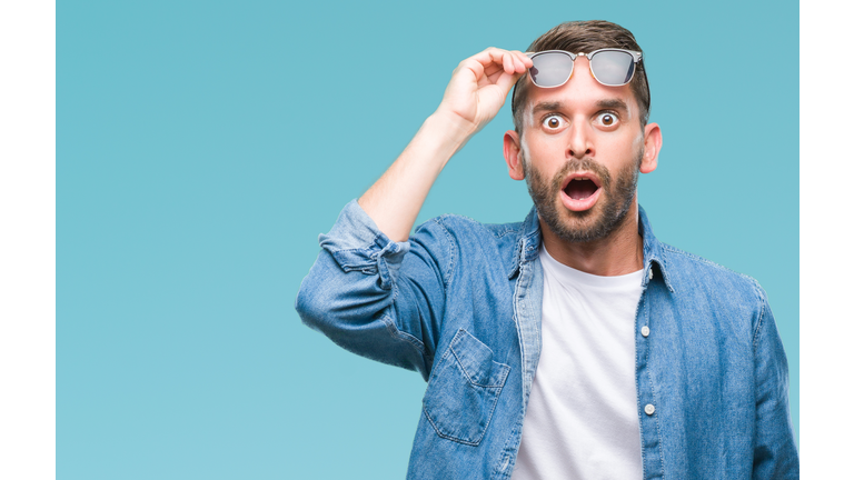 Young handsome man wearing sunglasses over isolated background afraid and shocked with surprise expression, fear and excited face.