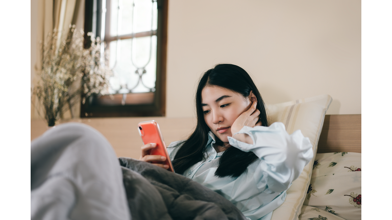 Young adult single woman using smartphone in the bed.