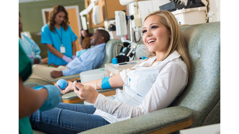 Woman donating blood in busy hospital donation bank