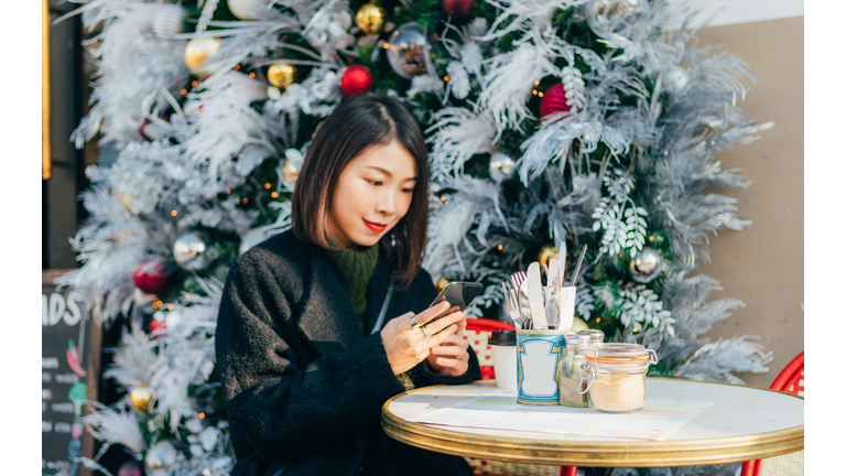 Young Woman With Smartphone Sitting At Sidewalk Cafe