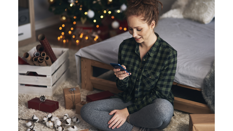 Woman texting while wrapping Christmas presents