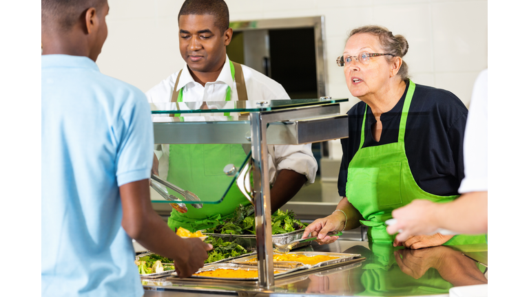 High school cafeteria lunchroom workers serving hot meal to students