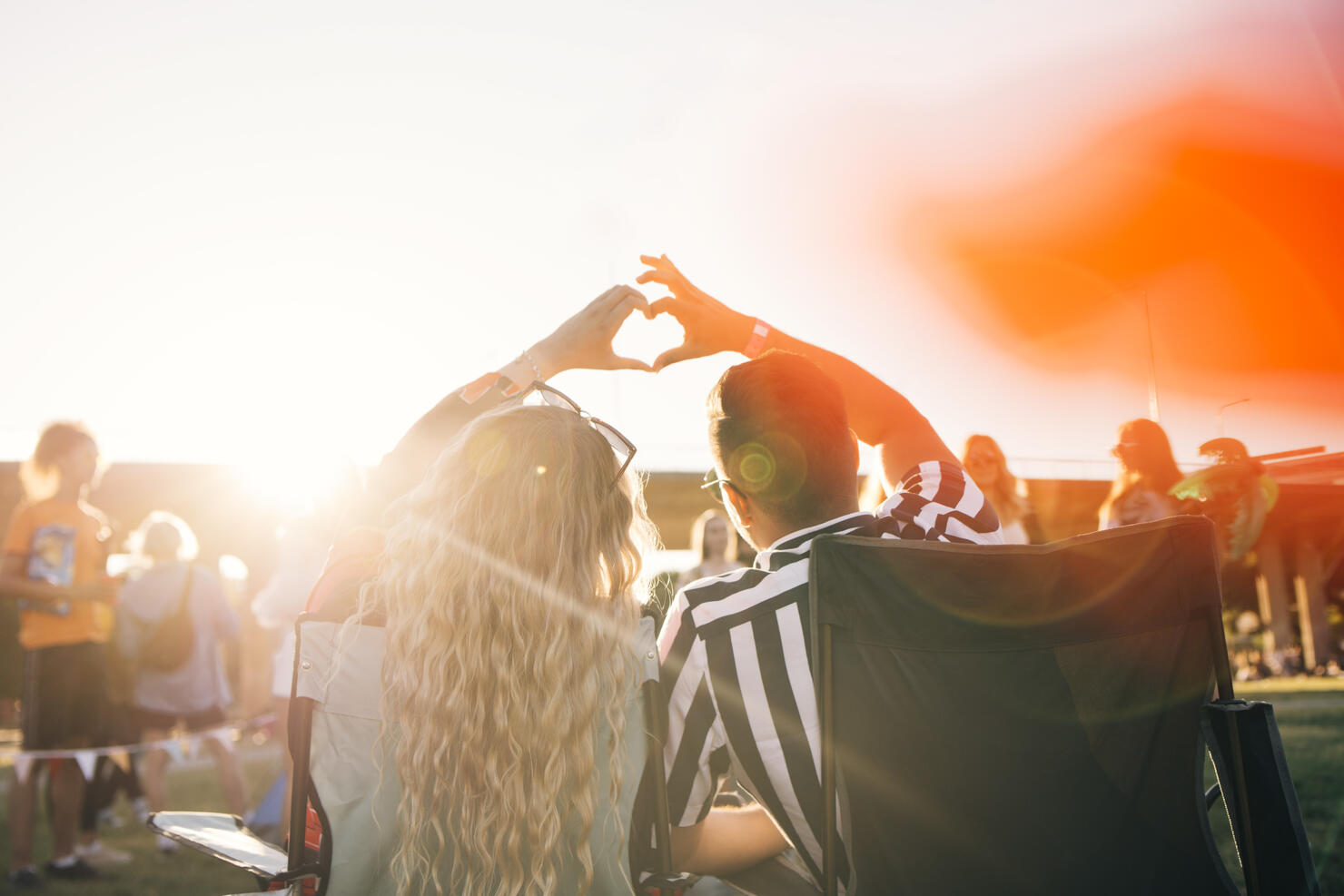 Rear view of couple making heart shape while enjoying in music festival on sunny day