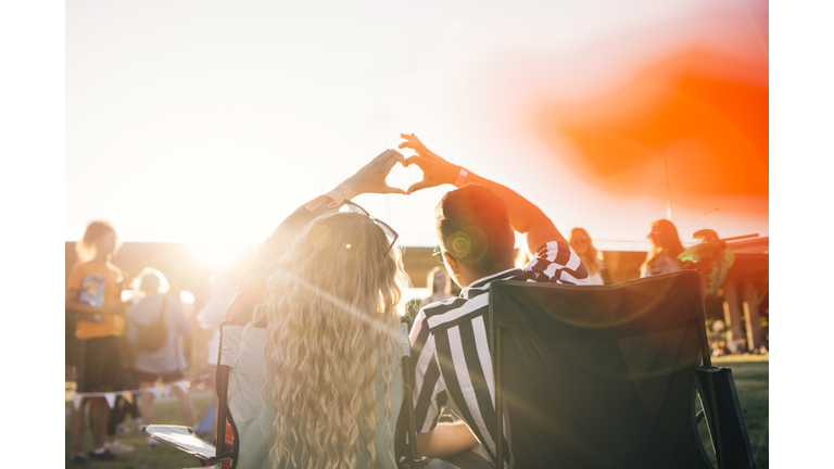 Rear view of couple making heart shape while enjoying in music festival on sunny day