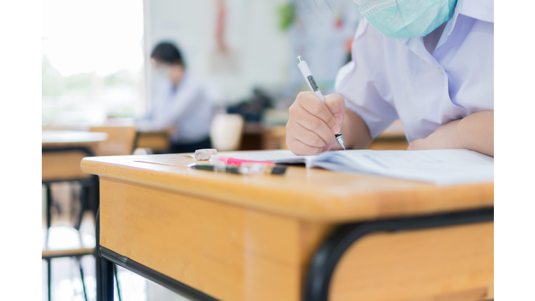 Asian Student girls wear face mask prevent COVID-19 coronavirus in Classroom for final test education exam room on High school. Students hold pencil writing paper documents for taking exams in room