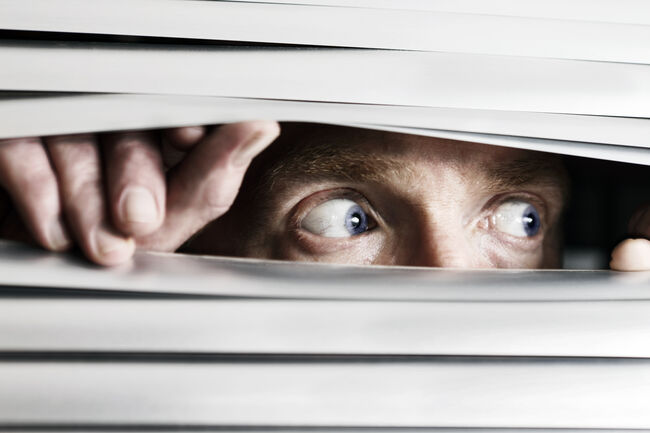 Fearful man looking sideways through venetian blind