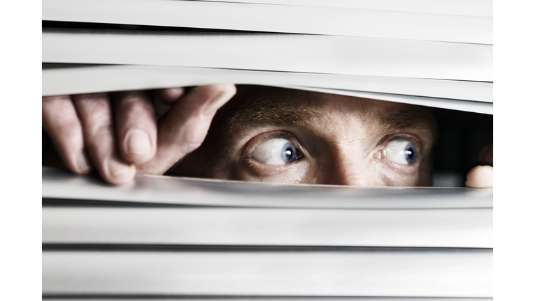 Fearful man looking sideways through venetian blind