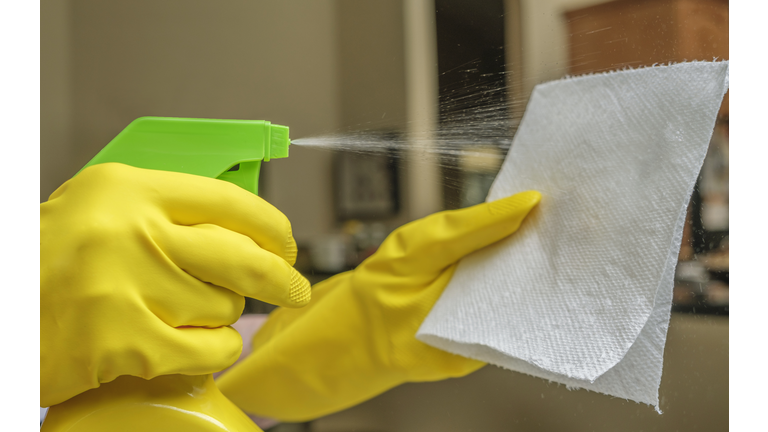 Close-up of gloved hand spraying disinfectant onto cleaning pad