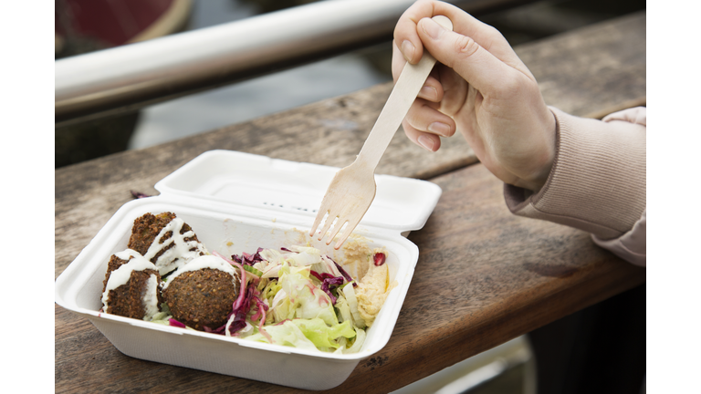 Close up of healthy food in take away box, hand holding fork at urban market.