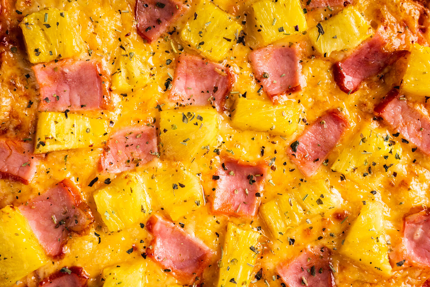 Just baked hawaiian pizza with freshly chopped pineapple and ham on the rustic wooden background. Selective focus.