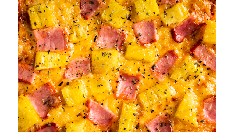 Just baked hawaiian pizza with freshly chopped pineapple and ham on the rustic wooden background. Selective focus.