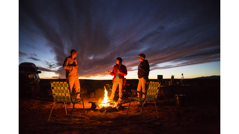 Three friends handing out at a campfire.