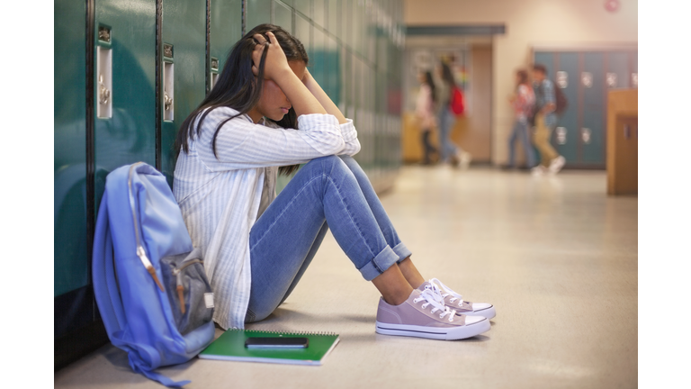 Frustrated Asian teenage young woman female student with head in hands in hallway in school