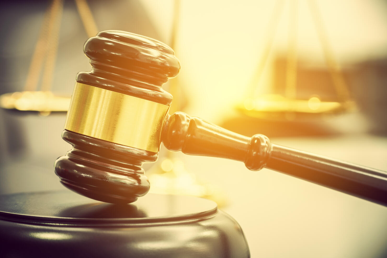 Legal office of lawyers, justice and law concept : Wooden judge gavel or a wood hammer and a soundboard used by a judge person on a desk in a courtroom with a blurred brass scale of justice behind.