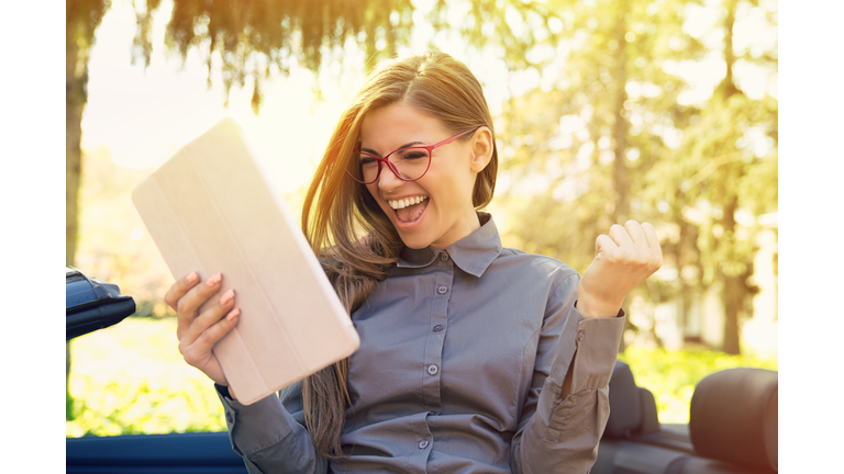 Cheerful woman standing by her new car searching job with pad computer