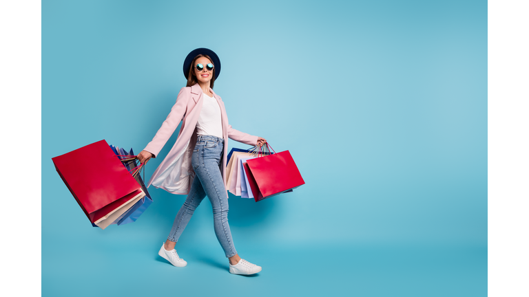 Full size photo of cute pretty cheerful lady in eyeglasses eyewear go shopping for bargains wear season cote denim jeans isolated over blue background