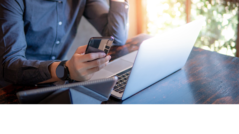 Male hand holding smartphone. Businessman using laptop computer and digital tablet while working in the cafe. Mobile app or internet of things concepts. Modern lifestyle in digital age.