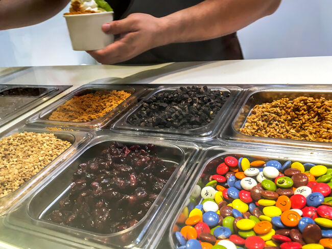Young men putting sweet toppings on frozen yogurt