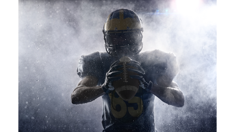 American football player in a haze and rain on black background. Portrait