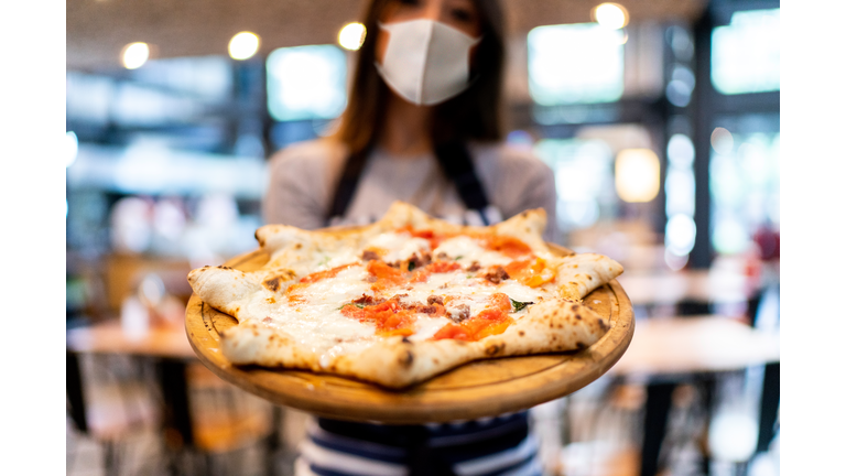 Waitress using protective mask showing pizza
