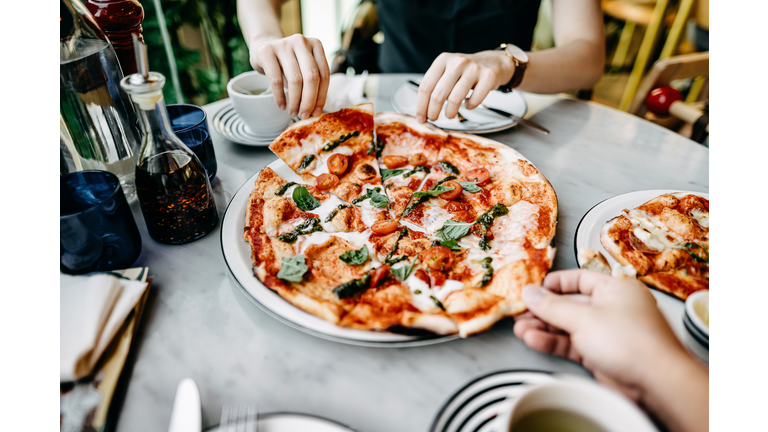 Close up of couple getting and sharing slices of freshly made pizza and enjoying meal in an Italian restaurant