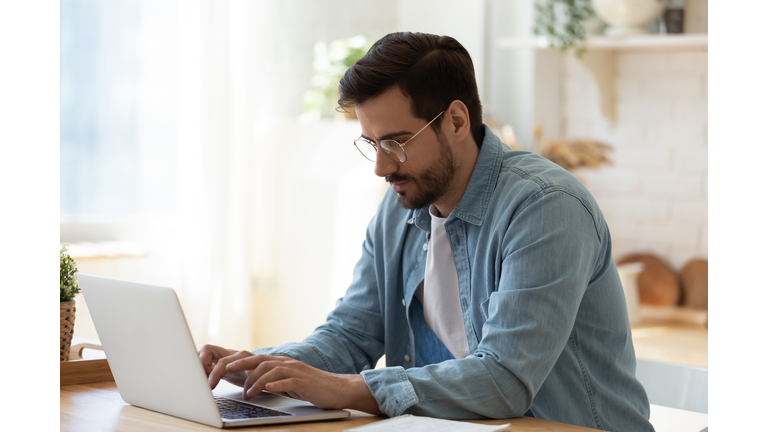 Handsome young businessman in eyewear working with computer remotely.