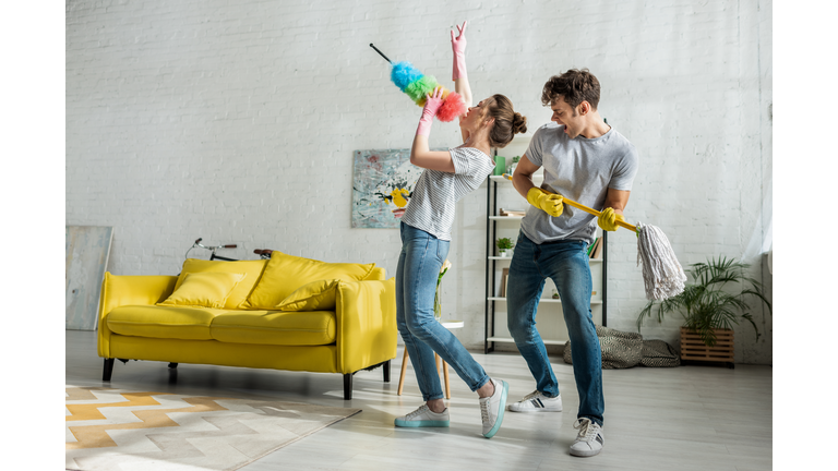 man and woman with household singing while doing spring cleaning in living room