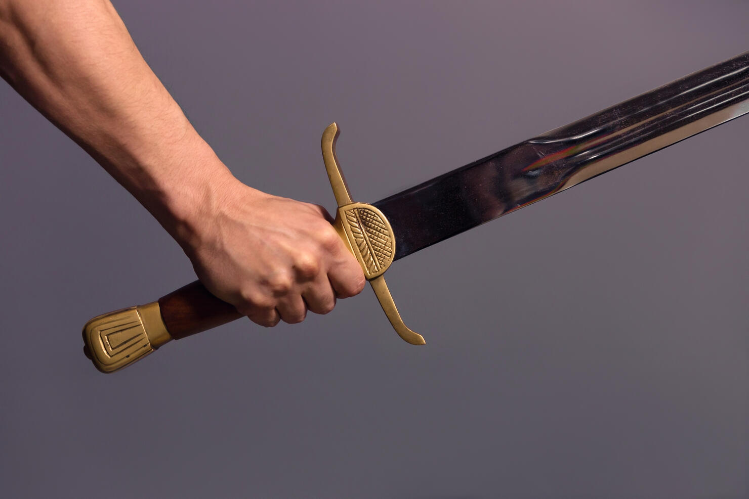 Cropped Hand Of Man Holding Sword Against Gray Background
