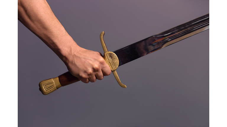 Cropped Hand Of Man Holding Sword Against Gray Background
