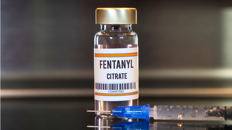 Fentanyl drug and syringe on black table with reflections and stainless background.