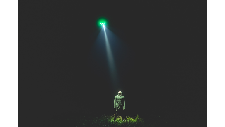 The UFO shines on a male standing on the grass. night time