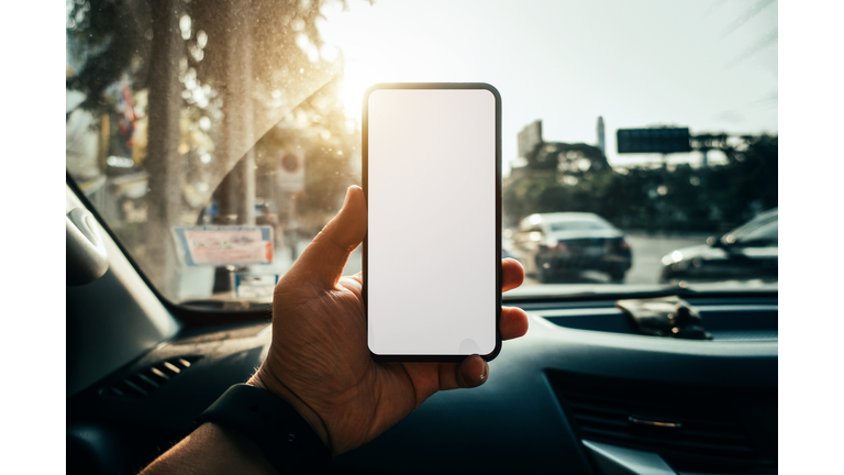 Close up of a man's hand using smartphone while travelling in a car against front window during traffic jam